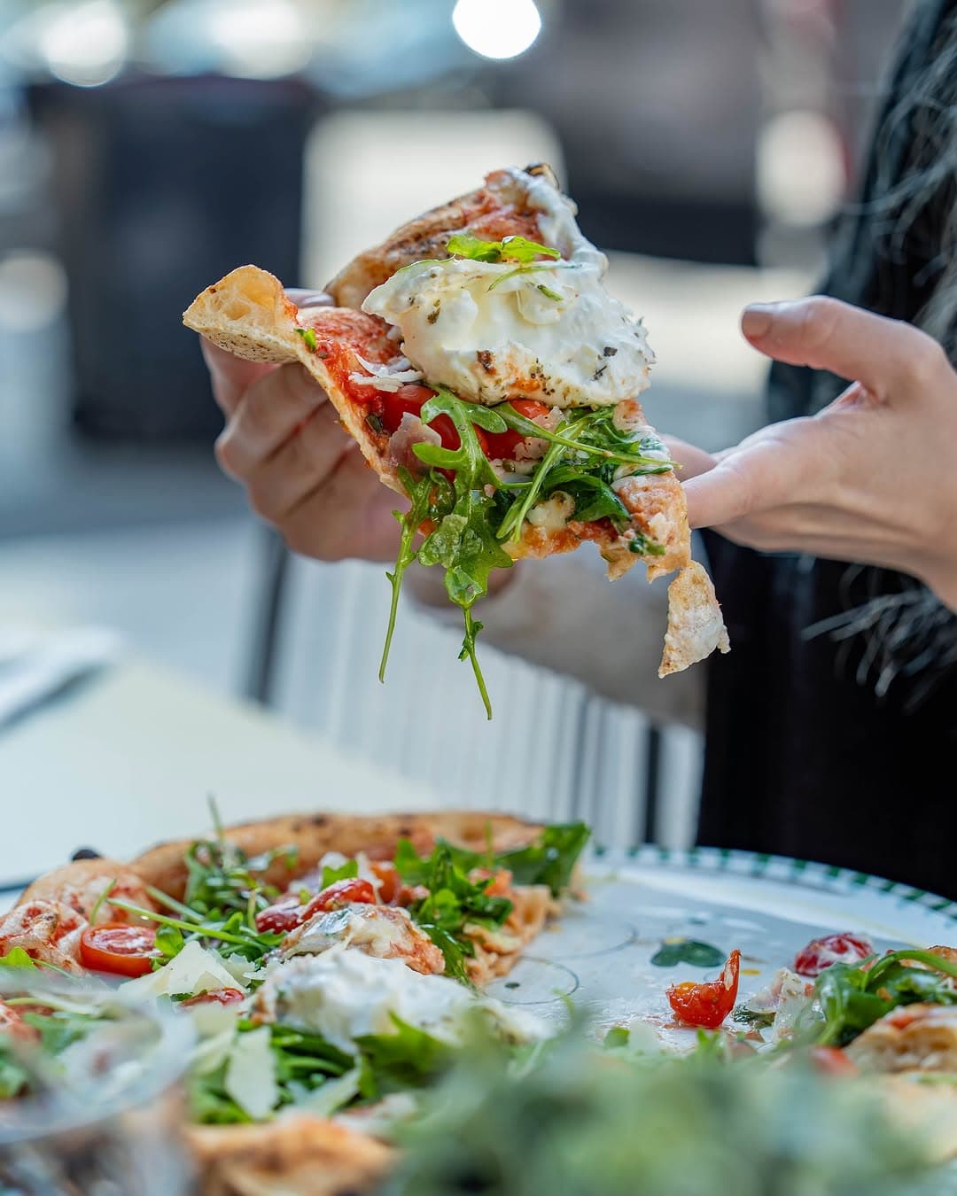 Pizza burrata roquette — part généreuse tenue en main, garnie de tomates cerises et mozzarella fondante
